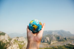 Man holding tiny globe in front of mountain landscape.