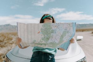Woman holding map outside in front of car.