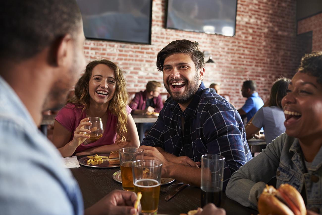 Friends Eating Out In Sports Bar With Screens In Background
